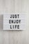 Lightbox with text `Just enjoy life` on a white wooden background, top view. Overhead, from above