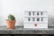 Lightbox with text STAY HOME and home plant in ceramic pot on wooden table. Stay safe, stay inside home concept