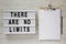 Lightbox with text `There are no limits`, clipboard with sheet of paper and pencil on a white wooden surface, top view