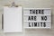 Lightbox with text `There are no limits`, clipboard with sheet of paper and pencil on a white wooden table, top view. Flat lay,