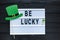 Lightbox with title Be lucky and photobooth green hat on wooden sticks at green background. Creative background to St. Patricks