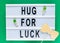 Lightbox with title Hug for luck and photobooth orange bow tie on wooden sticks at green background. Creative background