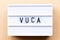 Lightbox with word VUCA abbreviation of Volatility, uncertainty, complexity and ambiguity on wood background