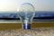 Lightbulb stands firm on the beach with water in the background