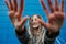 Lighthearted teenage girl blocking camera with hands in front of a blue panel