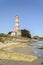 Lighthouse from the beach with seaweeds and waves breaker