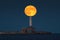 Lighthouse beacon and full moon twilight over sea horizon and moonlight in ripple water