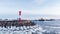 Lighthouse among breakwaters against sailing cargo ships