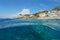 A lighthouse and buildings on a rocky coastline with a school of fish underwater, split view half above and below water surface