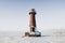 Lighthouse in a calm and desolate winter landscape. A white whitewashed lighthouse over blue sky with clouds