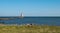 Lighthouse at end of pier, large boulders, green grass and driftwood at lake