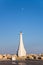 Lighthouse At The Entrance To The Marina On A Background Of Blue Sky With The Moon