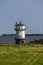 Lighthouse at the grassy shore on the background of wind turbines