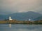 Lighthouse on Isle of Ornsay.Trade ship at rocky island, mountains in background.