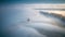 a lighthouse in the middle of a foggy field with trees in the distance and a body of water in the fo