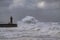 a lighthouse in the midst of a huge wave hitting some concrete