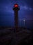 lighthouse on the seashore with red light at night against the background of the lights of the ships