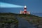 Lighthouse with shining light in darkness and dark blue clouds