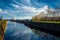 The lighthouse stands on the beach and canal, the blue sky with clouds and reflection in the water