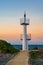 A lighthouse at sunset in Onna Son, Okinawa, Japan, with a calm sea and a glow from the setting sun