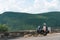 A lightly dressed girl is sitting on a motorcycle. No protection. Helmet. Sunny day in Narni, Italy. Green mountains in the