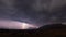 Lightning bolt and mountains in the distance with open field in the foreground.