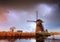 Lightning in cloudy dark sky. Traditional Dutch windmills canal