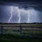 Lightning storm illuminates field with foreground fence, dramatic scene