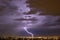Lightning streak from a thunderstorm cloud at night in a rural setting. There are multiple lightning strikes coming from the