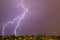 Lightning streak from a thunderstorm cloud at night in a rural setting. There are multiple lightning strikes coming from the