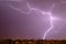 Lightning streak from a thunderstorm cloud at night in a rural setting. There are multiple lightning strikes coming from the