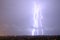 Lightning streak from a thunderstorm cloud at night in a rural setting. There are multiple lightning strikes coming from the