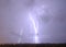 Lightning streak from a thunderstorm cloud at night in a rural setting. There are multiple lightning strikes coming from the