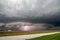 Lightning strikes as a supercell thunderstorm approaches a rural road.