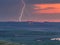 Lightning in the sunset sky over the hills with wind turbines and lake