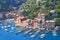 Liguria Portofino, view of harbor with moored boats and pastel colored houses lining the bay with trees on hills behind, Italy