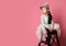 Liitle asian fashion kid girl in pink dress and funny cap with fur pompon sits on a ladder and looks on free text space