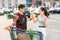 Likable asian couple standing near shopping cart,man holds pineapple and melon and beautiful woman counts the banknotes