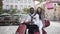 Likable joyful mixed races couple sitting on the scooter and girl holding in her hands purchases on the background of