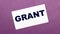 On a lilac background, a white card with the word GRANT