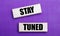 On a lilac bright background, light wooden blocks with the text STAY TUNED
