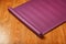 A lilac-colored yoga mat is spread out in a roll on the wooden floor.