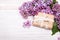 Lilac flowers and cute gift box on white wooden background,