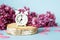 Lilac flowers with vintage tiny alarm clock on blue background. Spring time morning concept