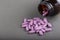 Lilac medical pills are falling out of a bottle on a gray background. Concept of health, drug addiction