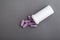 Lilac medical pills are falling out of a white bottle on a gray background. Concept of health, drug addiction