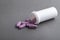 Lilac medical pills are falling out of a white bottle on a gray background. Concept of health, drug addiction