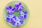 Lilac violet flowers lie on a green saucer on a yellow background. Top view, mock up, copy space. Postcard idea