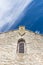 Limestone facade of ancient church with window shutter and cross