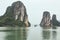 Limestone islands on left and right side over emerald water with tourist boats cruising pass defile of islands with bright sky.